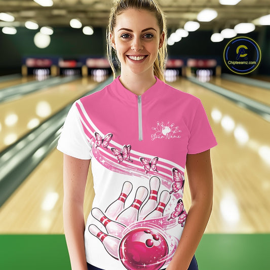 Female model wearing a white and pink bowling quarter zip with butterfly artwork and bowling graphics, front view inside a bowling alley