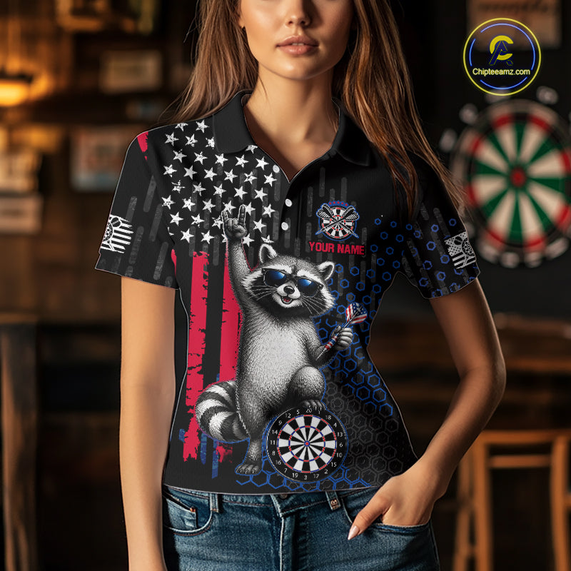 A woman wearing a custom patriotic dart polo shirt featuring an American flag raccoon holding darts beside a dartboard in a professional dart room.