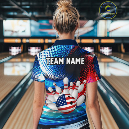 A woman viewed from behind wearing a short-sleeve bowling-themed polo shirt with a patriotic red, white, and blue design featuring bowling pins, a bowling ball with an American flag pattern, and the text 'TEAM NAME'. The background shows a blurred bowling alley with lanes and pins.