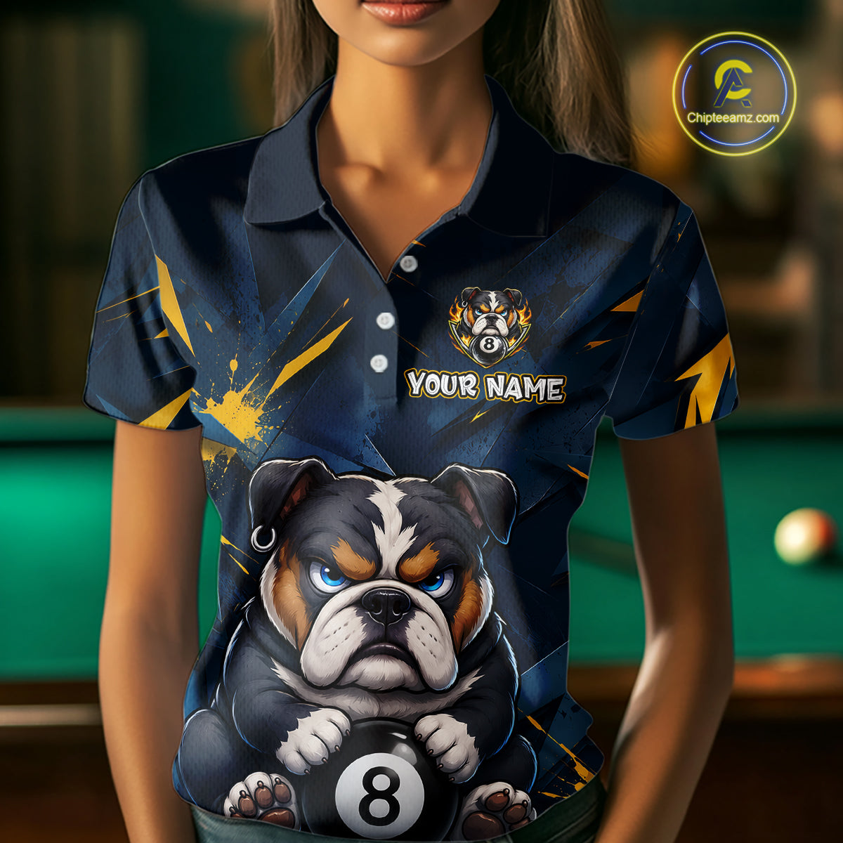 A front view of a custom blue and yellow billiards polo shirt worn by a female model . The shirt features  a cartoon bulldog with its paw on an 8-ball on the front. A 'YOUR NAME' text placeholder . The background is a blurred billiards room with a green pool table.
