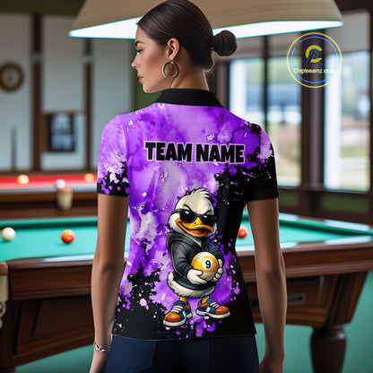 A woman stands in a billiards room wearing a custom short-sleeve polo shirt from the back. The shirt features a vibrant purple and black paint splatter design with a cartoon duck mascot holding a pool ball and the text 'TEAM NAME'.
