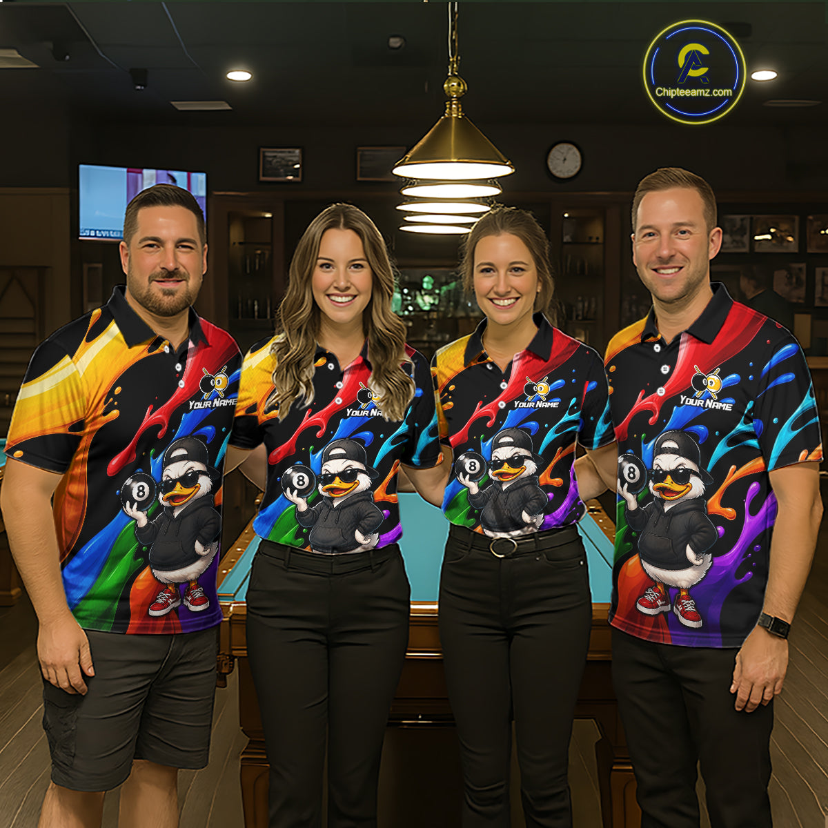 Four people standing together in a dimly lit bar or lounge, wearing matching colorful graphic polo shirts with cartoon duck artwork and the text 'Your Name'. The shirts feature a rainbow gradient and a large duck illustration on the front.
