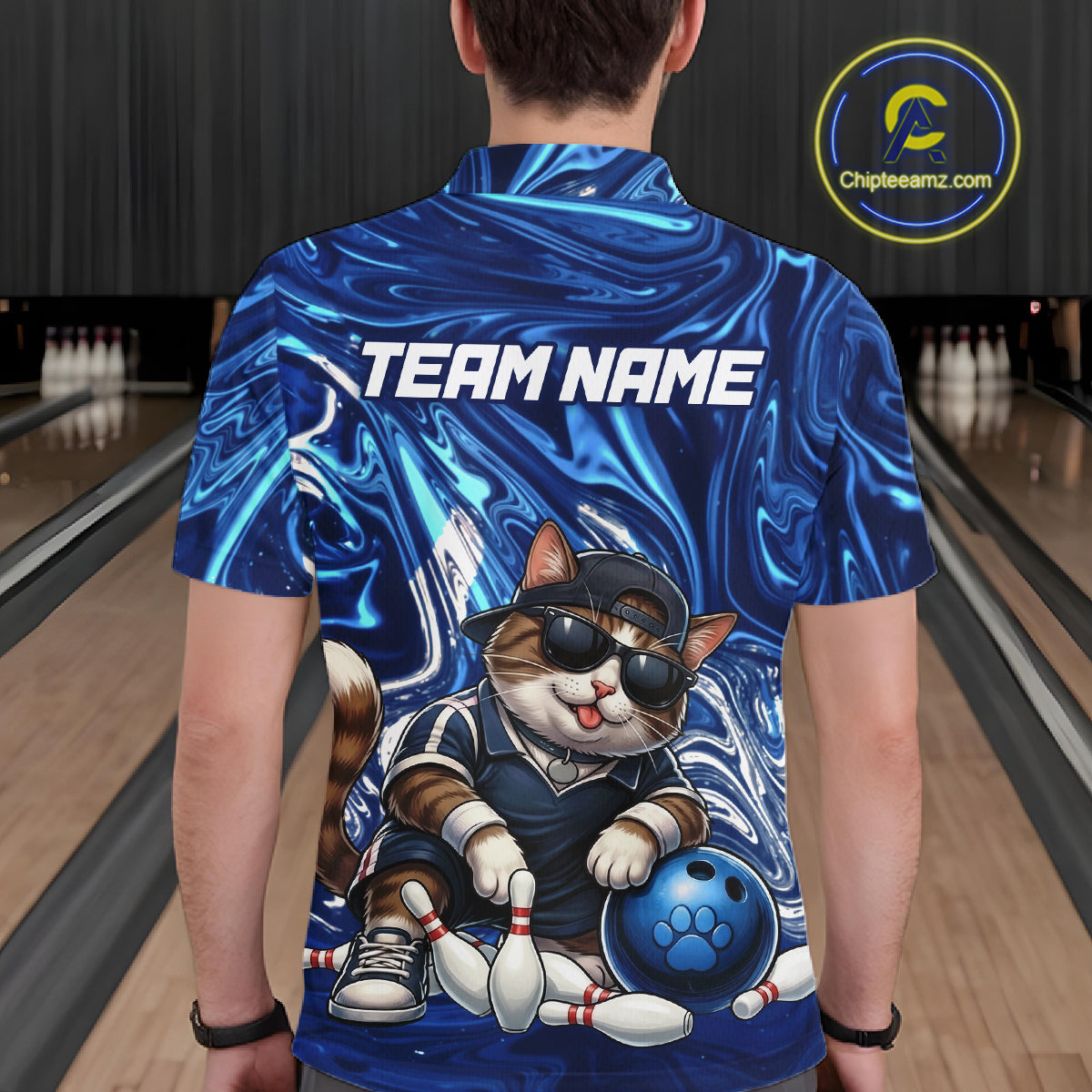 Person wearing a blue bowling shirt with a cat graphic and 'TEAM NAME' text in a bowling alley.