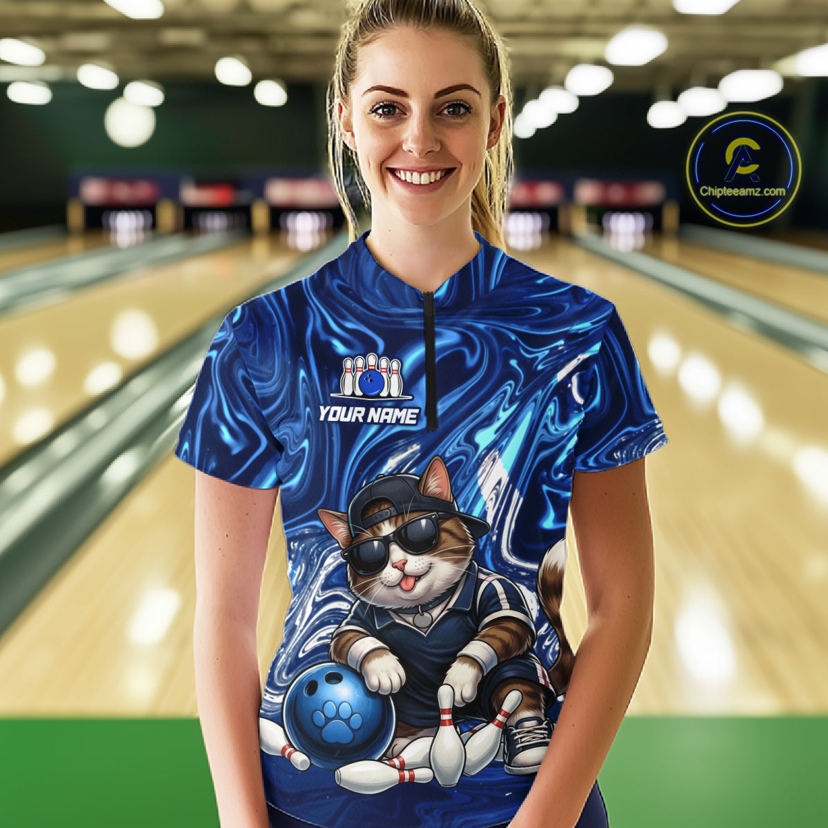 Person wearing a blue bowling shirt with a cat design in a bowling alley.