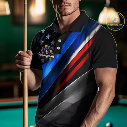 A man in a poolroom wearing a black polo shirt with a diagonal American flag-inspired design featuring blue, red, white, and gray stripes, plus a stars-and-stripes chest graphic with billiard balls and the text 'YOUR NAME'. He is holding a pool cue.