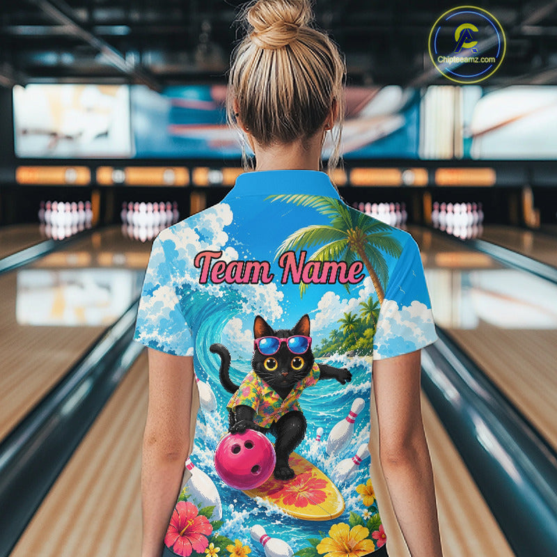 A woman viewed from behind wearing a short-sleeve bowling-themed shirt with a colorful back print featuring a black cat surfing on a yellow board, palm trees, flowers, and the text 'Team Name'. The background shows blurred bowling lanes in an indoor bowling alley.