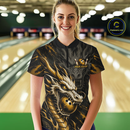 A woman wearing a black and gold bowling-themed long-sleeve polo shirt with a dragon graphic, standing in a bowling alley. The shirt features a black collar and a black body with a large gold and black dragon design wrapping around the front, with a small 'YOUR NAME' customization option on the chest.
