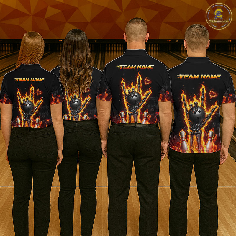 Four people standing in a bowling alley, viewed from behind, wearing matching black short-sleeve shirts with a large fiery bowling graphic on the back and 'TEAM NAME' printed across the shoulders.