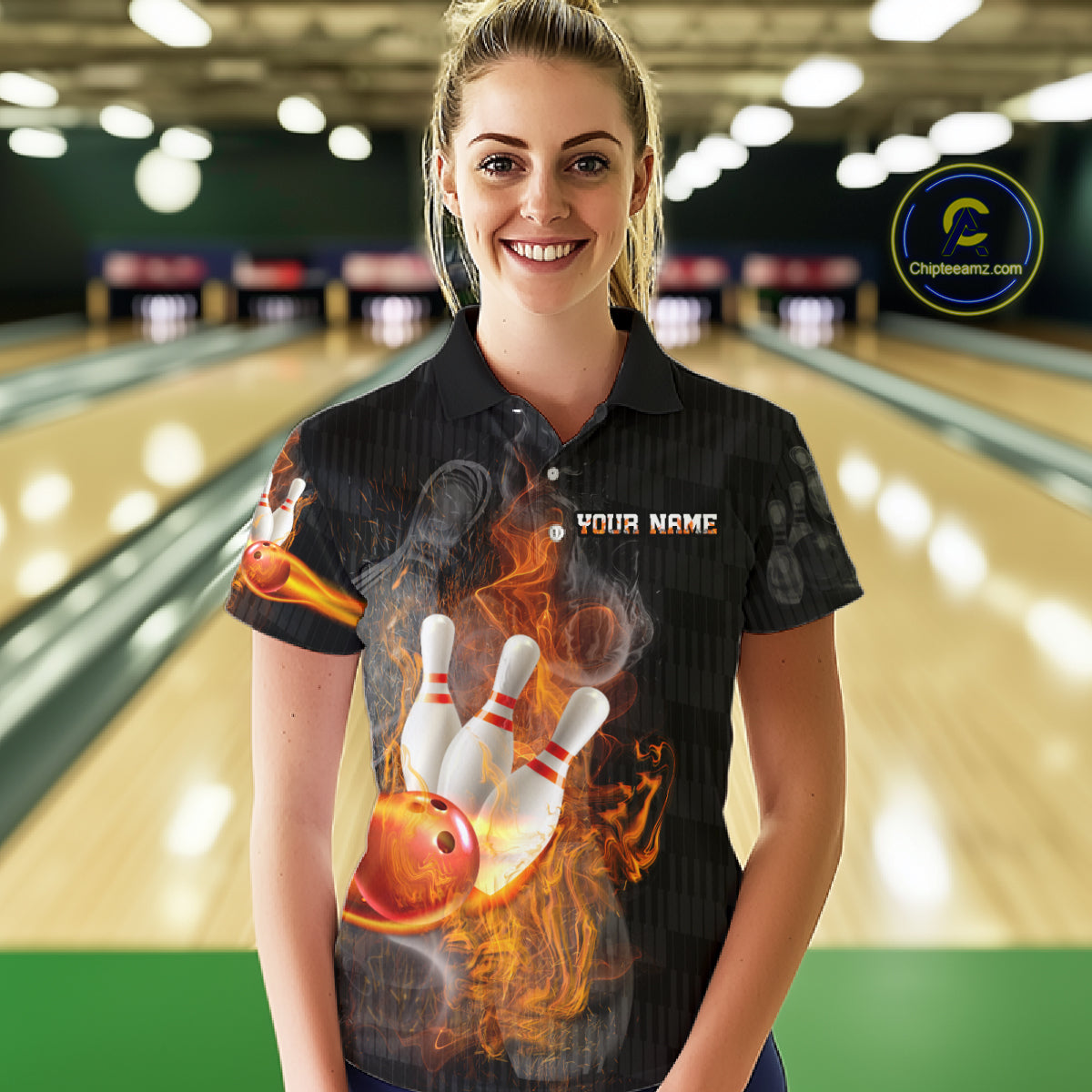 A woman wearing a black short-sleeve polo shirt with a bowling-themed flame graphic on the front, standing in a bowling alley. The shirt features a large bowling ball and pins design with the text 'YOUR NAME' on the chest.
