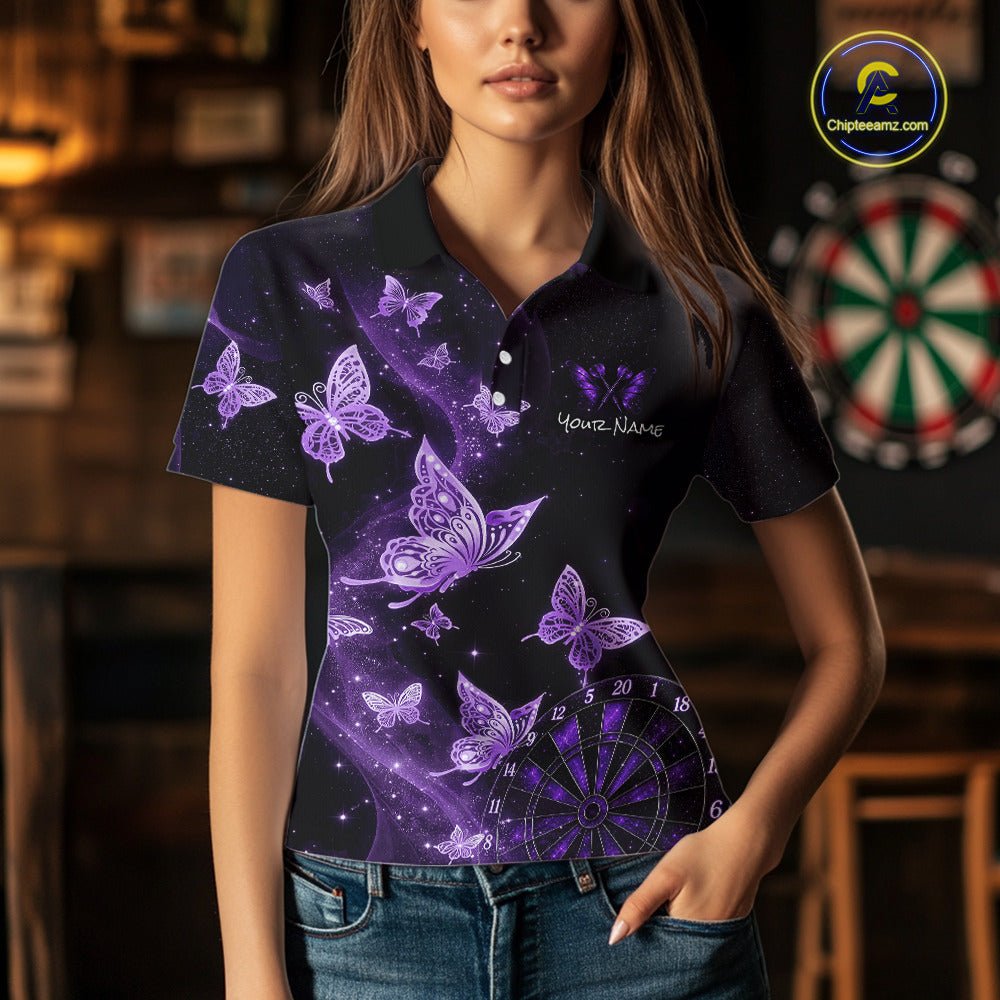 A woman wearing a short-sleeve polo shirt with a purple and black butterfly and galaxy print, standing in a dimly lit bar environment with a dartboard in the background.