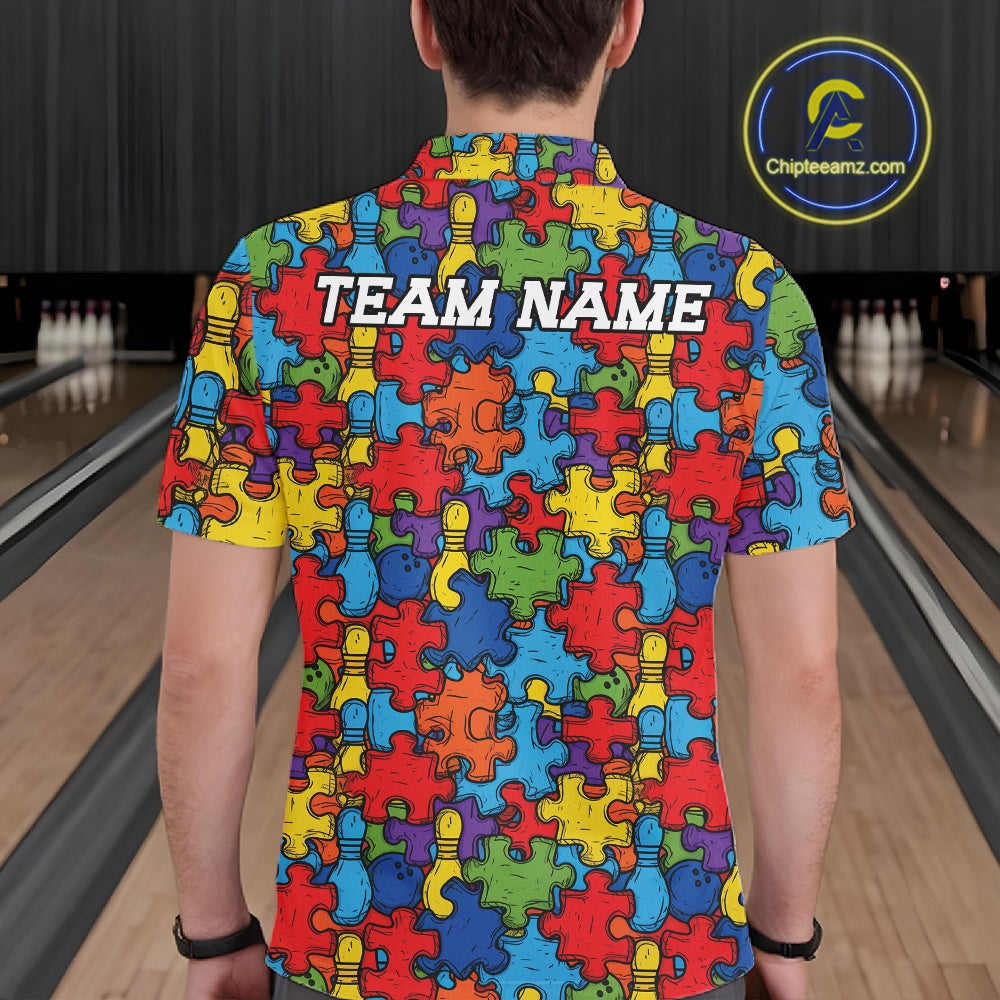 A man viewed from behind wearing a short-sleeve shirt with a colorful autism awareness puzzle-piece pattern and the text 'TEAM NAME' printed across the upper back. The background shows a bowling alley with lanes and pins.