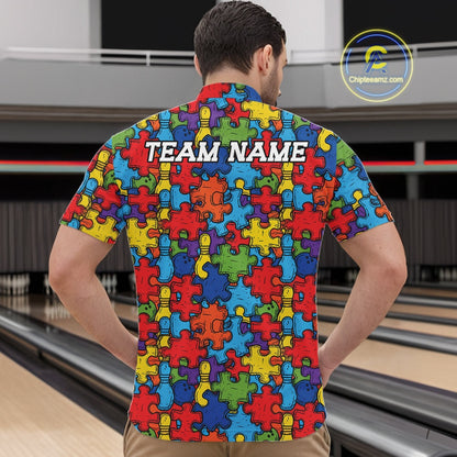 A man viewed from behind wearing a short-sleeve  shirt with a colorful puzzle-piece pattern and the text 'TEAM NAME' printed across the upper back. Bowling alley lanes are visible in the background