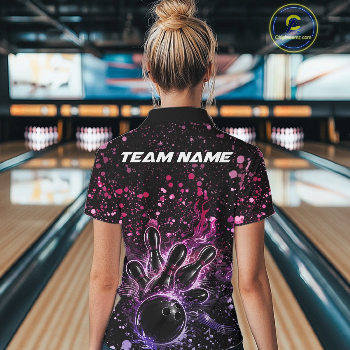 Back view of a female model in a black bowling quarter-zip shirt displaying bowling strike graphics with pink and purple paint splatters.