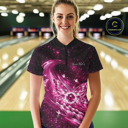Female model shown from the front in a bowling center wearing a pink quarter-zip shirt with luminous butterfly wings and bowling ball graphics.