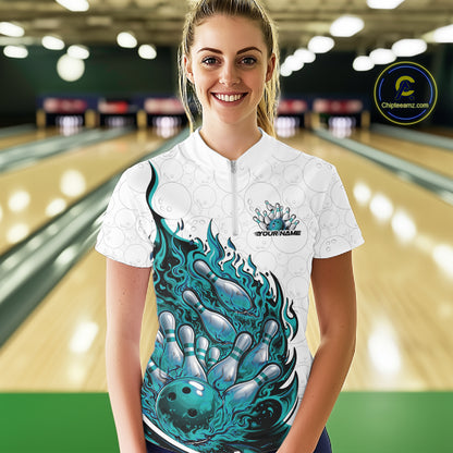Front view female model at bowling lane wearing white and turquoise blue quarter zip shirt showing flaming bowling ball crashing into pins with vivid fire illustration.