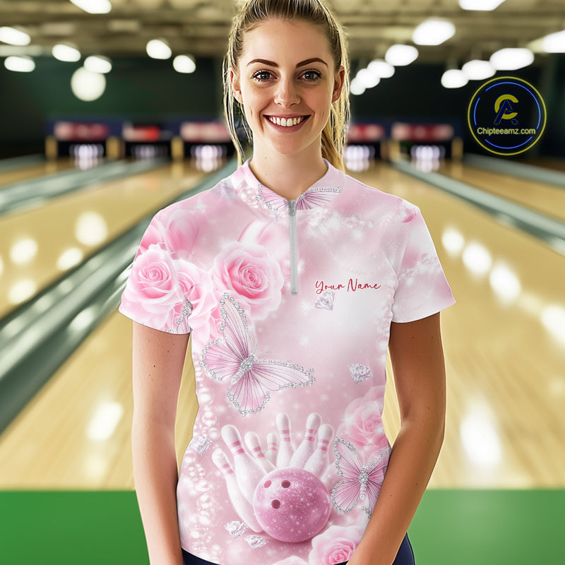 Female model shown from the front in a bowling center wearing a quarter-zip shirt featuring pink glitter butterflies, roses, bowling pins, and a bowling ball.