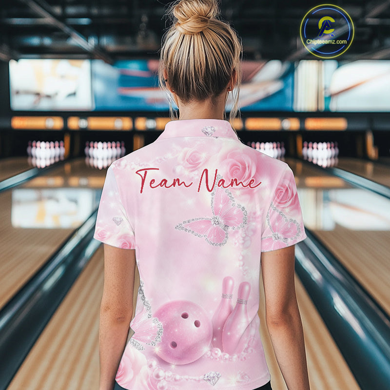 Back view of a female model in a bowling alley wearing a bowling polo shirt featuring pink glitter butterflies, roses, bowling pins, and a bowling ball design.