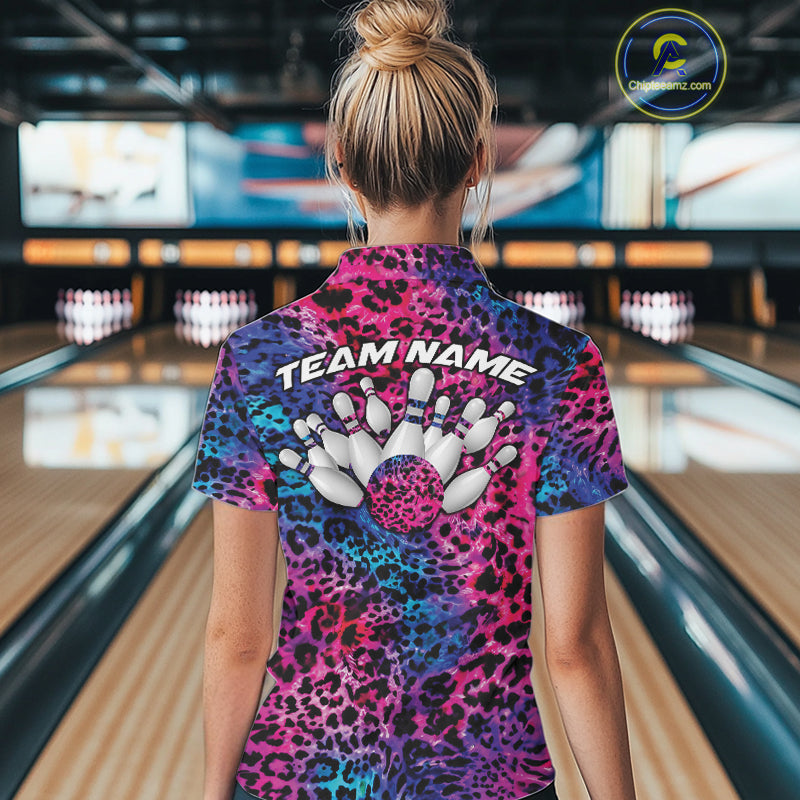 Back view of a woman standing at a bowling alley, wearing a purple, blue, and black leopard-print bowling polo with “Team Name” and bowling pins on the back.