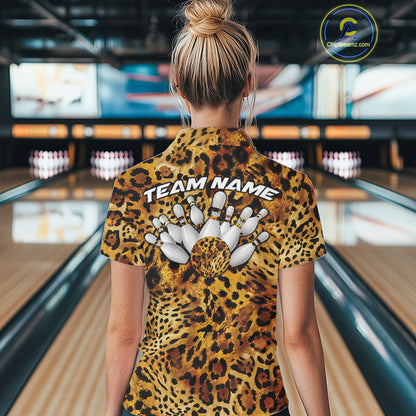 Back view of a woman standing at a bowling alley, wearing a gold, brown, and black leopard-print bowling polo with “Team Name” and bowling pins on the back.
