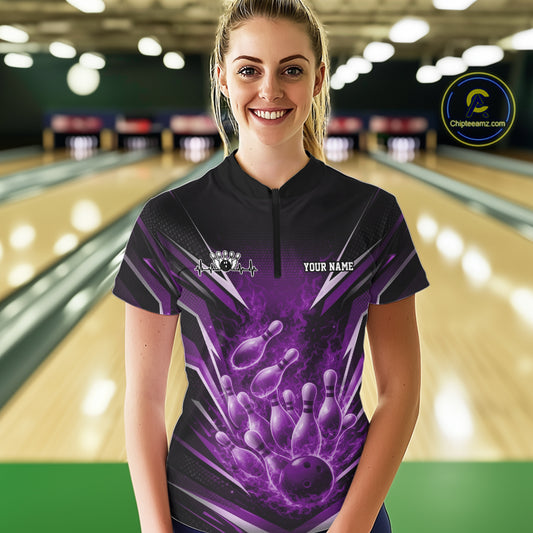 Front view female model in bowling lane wearing black and purple quarter zip shirt featuring flaming bowling ball striking pins with vivid fire action illustration.