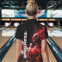 Load image into Gallery viewer, Back view of a female model in a bowling alley wearing a black bowling polo shirt featuring a red fiery skull with lightning striking a bowling ball and pins and a custom name.
