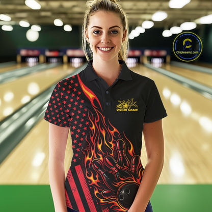 Female model at a bowling lane wearing a black bowling polo shirt with red-orange flame bowling strike artwork and patriotic graphics.