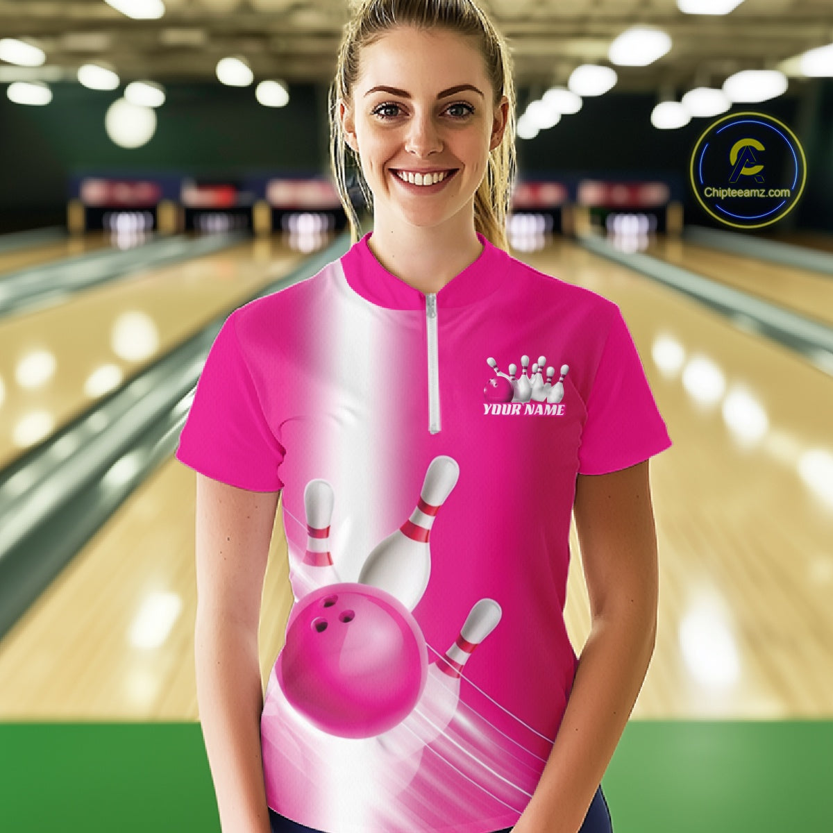 Front view female model at the bowling lane wearing a quarter zip shirt with bowling ball and pins flowing across a pink gradient design.