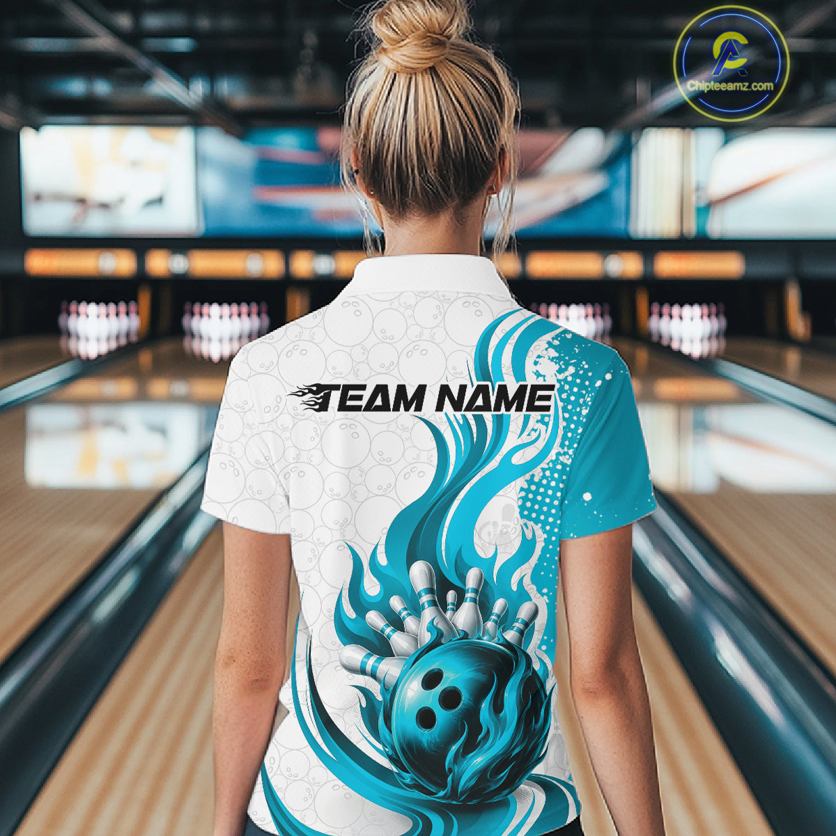 A woman viewed from behind wearing a custom bowling-themed short-sleeve collared shirt with a white and teal flame design and a bowling ball graphic on the back, standing in a bowling alley.
