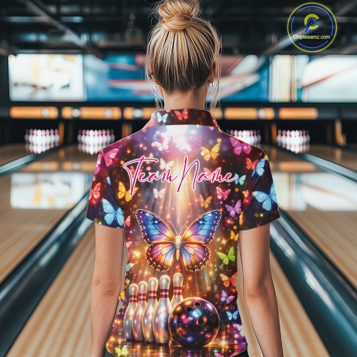 Back view of a female model in a bowling venue wearing a bowling quarter-zip shirt showcasing colorful butterfly artwork and bowling-themed graphics.