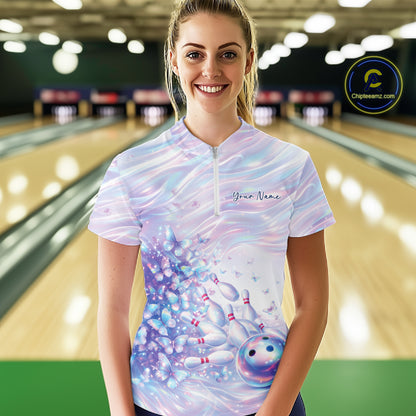 Female model wearing a bowling quarter zip with pastel purple and pink holographic butterfly graphics and bowling accents, front view at the bowling lane