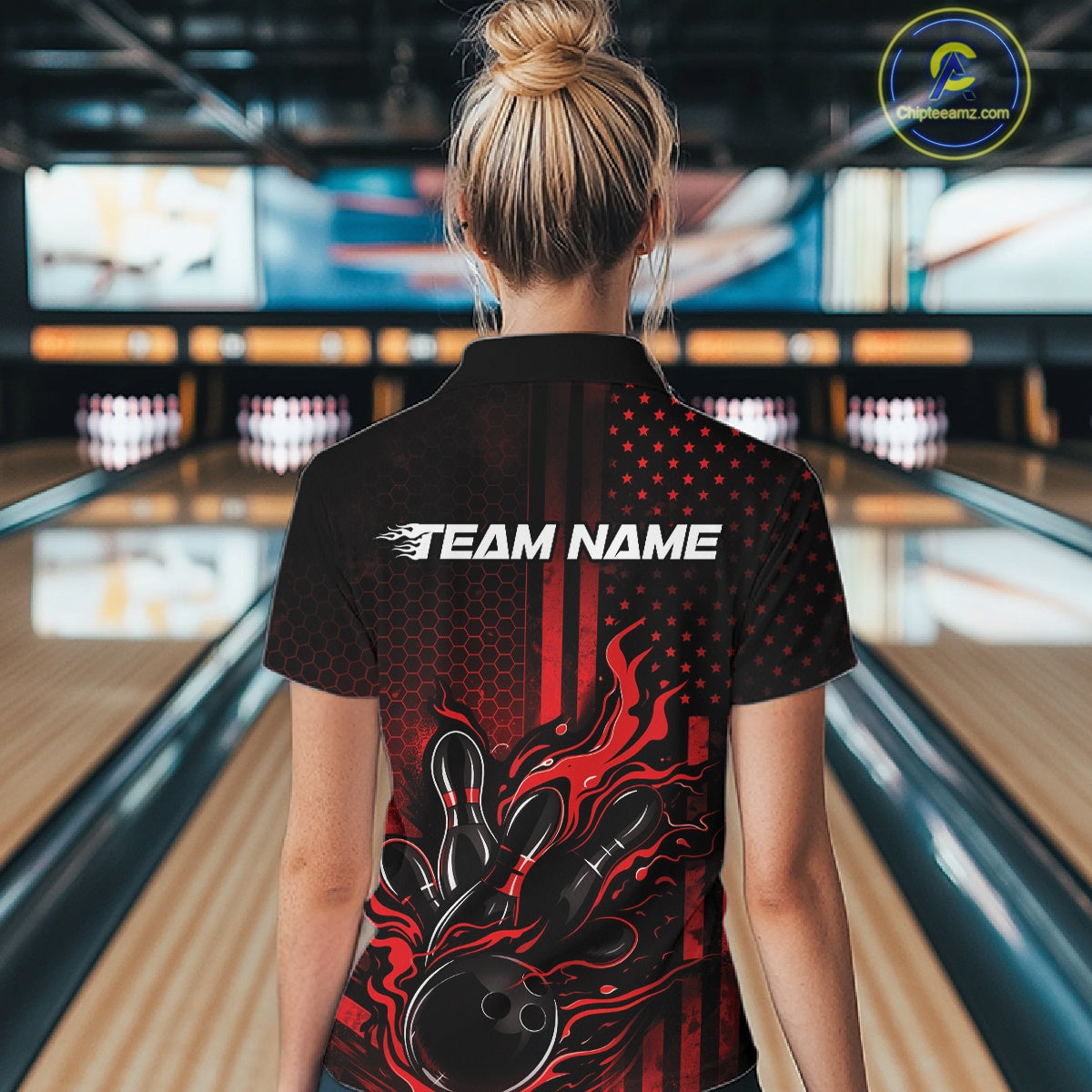Back view of a female model in a bowling alley wearing a black and red polo featuring bowling pins and flaming bowling ball artwork.