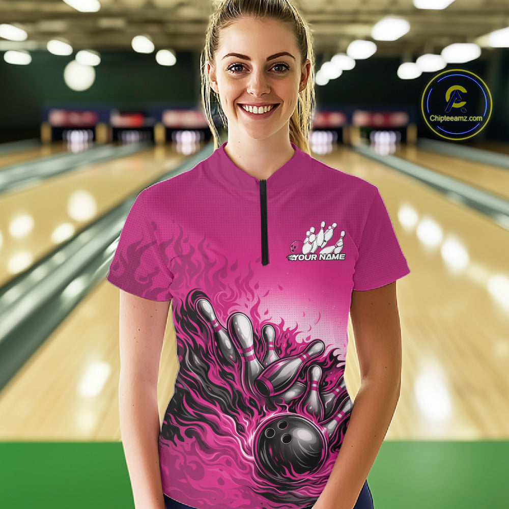 Female model in a bowling lane wearing a pink quarter-zip shirt, flame bowling ball striking pins with energetic sports graphics.
