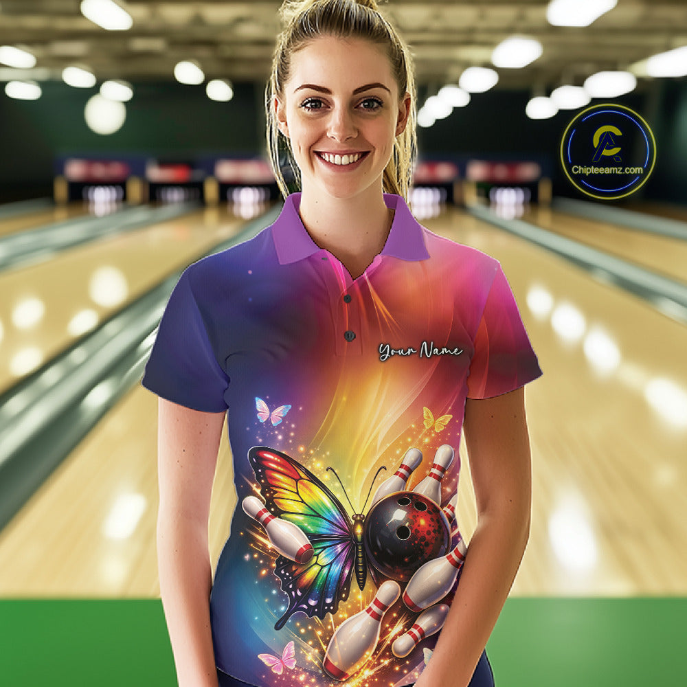 Female model at a bowling lane wearing a bowling polo shirt with a rainbow butterfly, bowling ball, and scattered pin artwork.