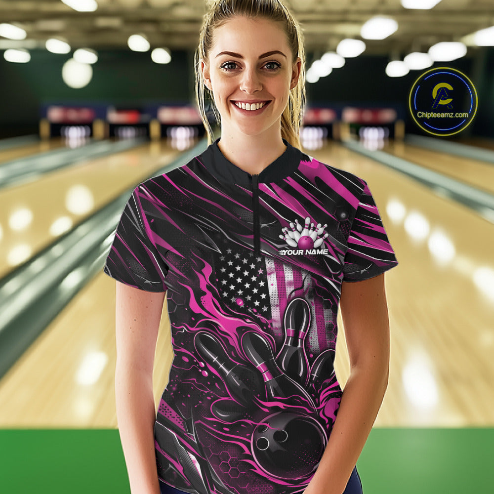 Female model in a bowling lane wearing black and pink quarter zip shirt, front view showcasing patriotic flames bowling ball hitting pins with energetic styling