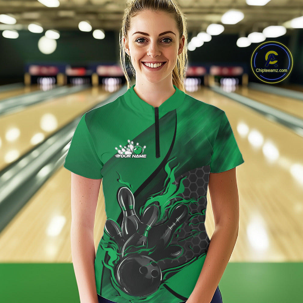 Female model in a bowling lane wearing black and green quarter zip shirt, front view featuring flaming bowling ball striking pins with hexagon design