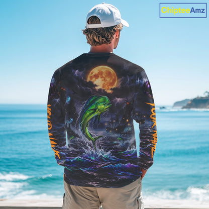 A man stands with his back to the camera wearing a long-sleeve graphic shirt featuring a green fish jumping in front of a full moon over the ocean. The shirt has orange text down the sleeves and is shown against a beach background with a 'ChipteeAmz' watermark in the top right corner.