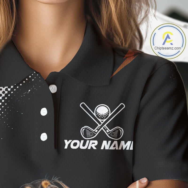 A close-up of a person wearing a black polo shirt with a white golf-themed graphic on the chest featuring crossed golf clubs, a golf ball, and the placeholder text 'YOUR NAME'.