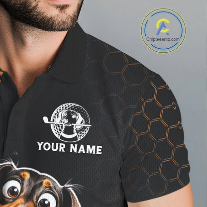 A close-up of a man wearing a black short-sleeve polo shirt with a custom graphic print. The shirt features a white circular dog golf logo and the text 'YOUR NAME' on the chest, a subtle gold hexagonal pattern on the right sleeve, and a cartoon dog face graphic at the bottom left.
