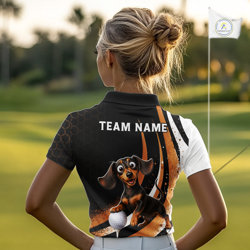 A woman on a golf course seen from behind, wearing a custom black and white short-sleeve polo shirt with a cartoon dachshund graphic and 'TEAM NAME' printed on the back.