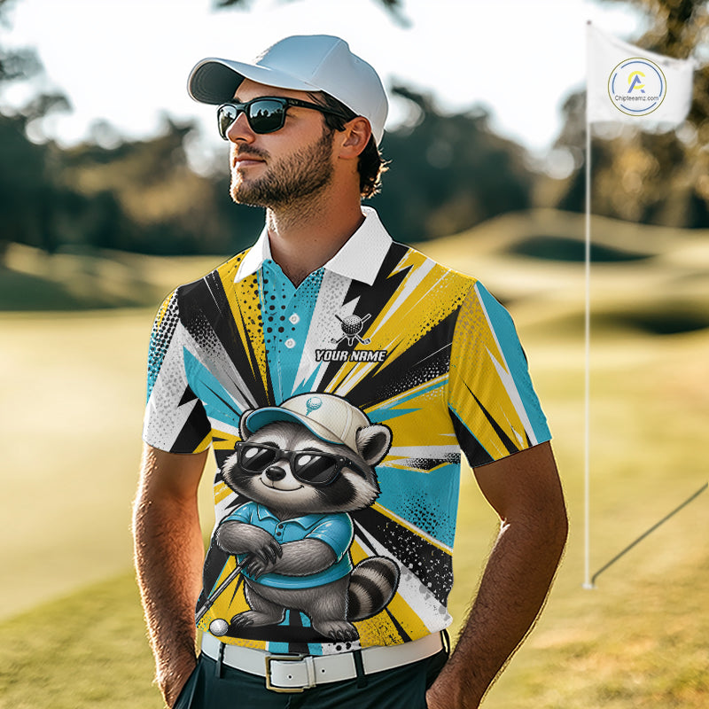 A man wearing a custom printed short-sleeve polo shirt with a raccoon graphic, standing on a golf course. The shirt features a bold geometric pattern in yellow, blue, black, and white, with a cartoon raccoon wearing a golf hat and sunglasses on the front.