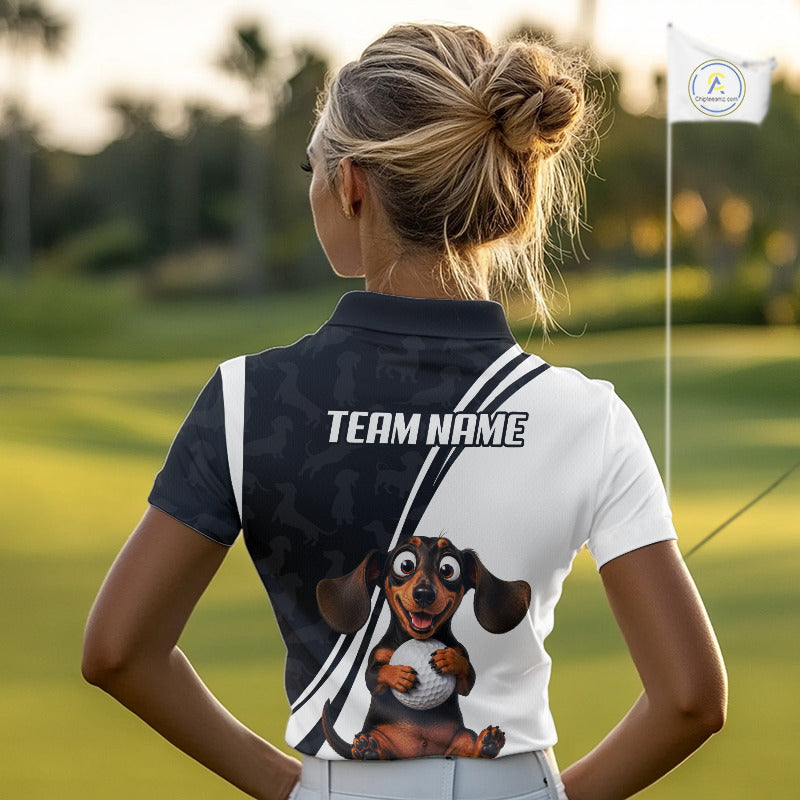 A woman on a golf course seen from behind, wearing a custom short-sleeve polo shirt. The shirt is split vertically down the center with a dark navy/black side featuring a subtle dog pattern and the text 'TEAM NAME', and a white side featuring a cartoon dachshund holding a golf ball.