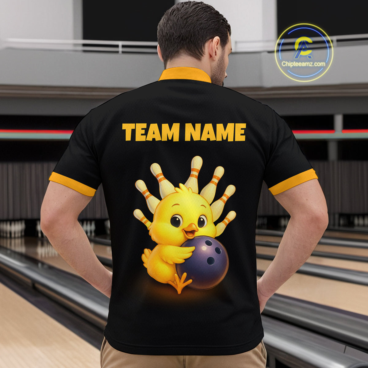 Person wearing a black shirt with a yellow chick holding a bowling ball design and 'TEAM NAME' text, in a bowling alley.